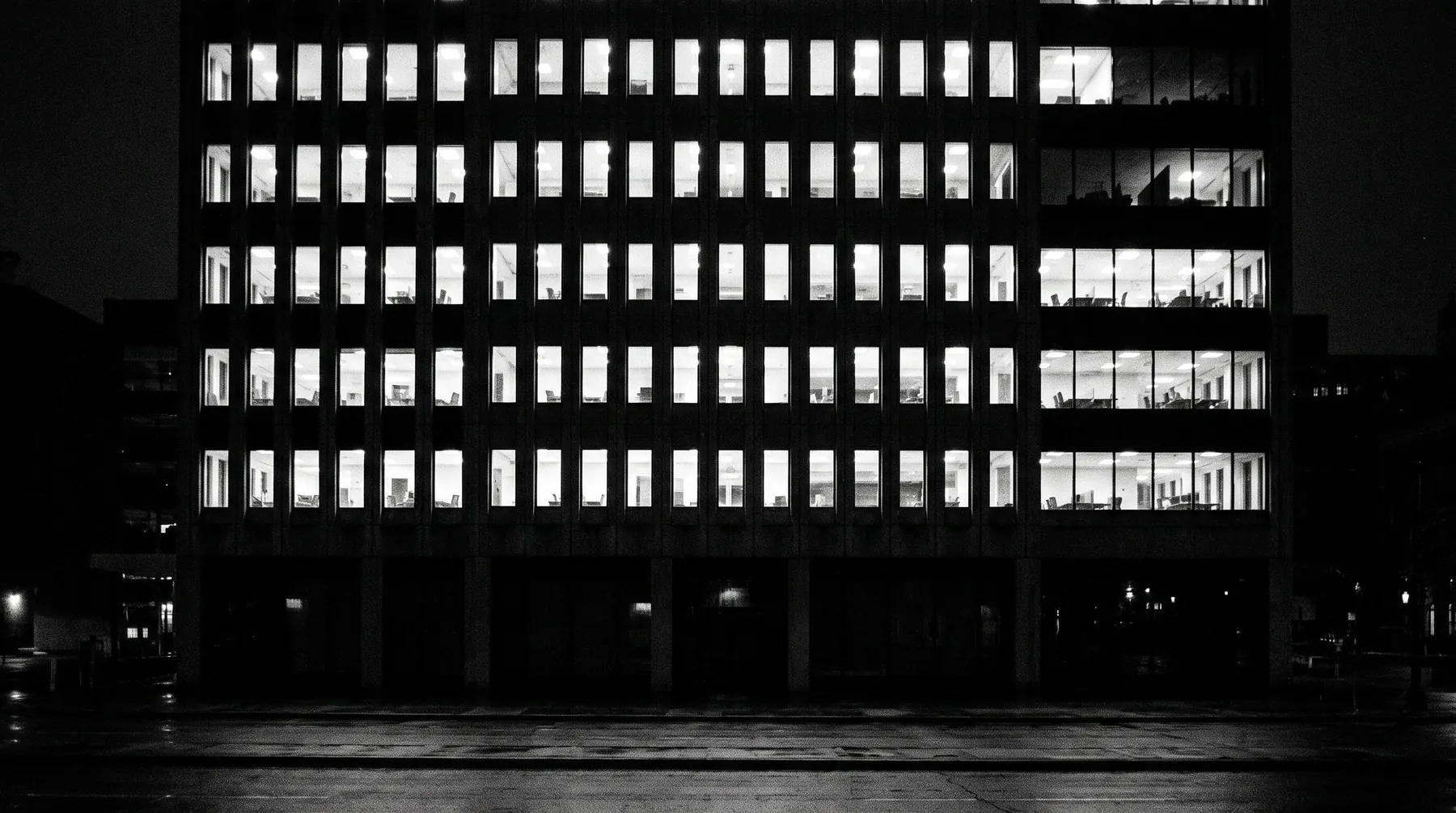 Façade d’immeuble de bureaux la nuit, fenêtres éclairées, aucun occupant